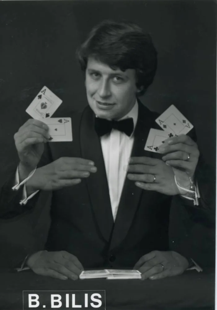 Photo promotionnelle en noir et blanc de Bernard Bilis en smoking : quatre mains montrent les quatre as au-dessus d'un jeu étalé, sous le bandeau « B. BILIS »