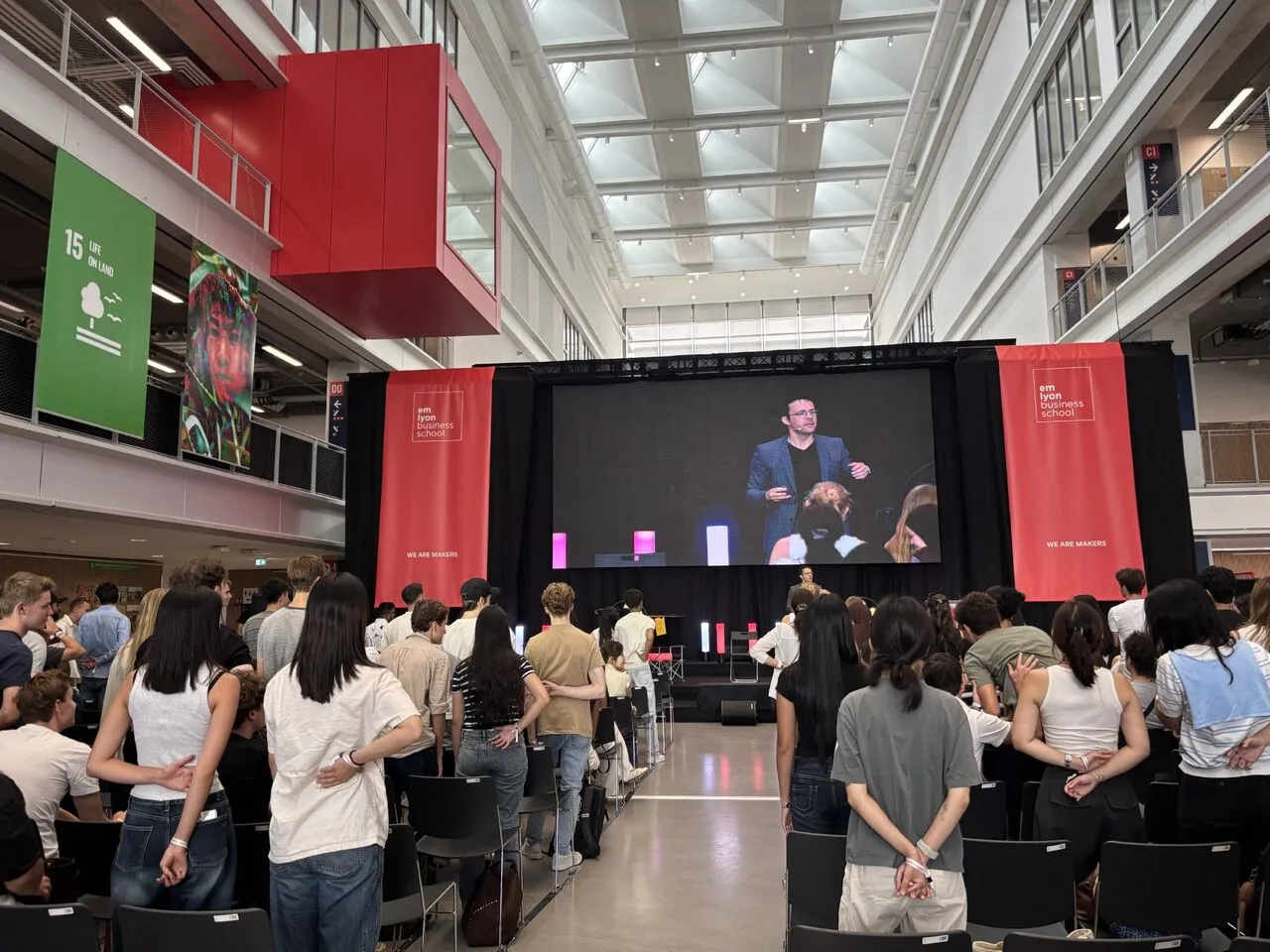 Le public international de l'emlyon Business School debout, mains dans le dos, pendant une expérience collective de mentalisme