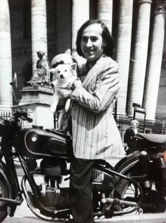 Garcimore en veste rayée, debout près d'une moto ancienne, sa chienne Dolly dans les bras