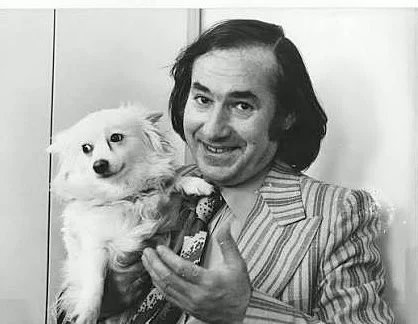 Portrait en noir et blanc de Garcimore souriant, en veste rayée, tenant sa petite chienne blanche Dolly dans ses bras