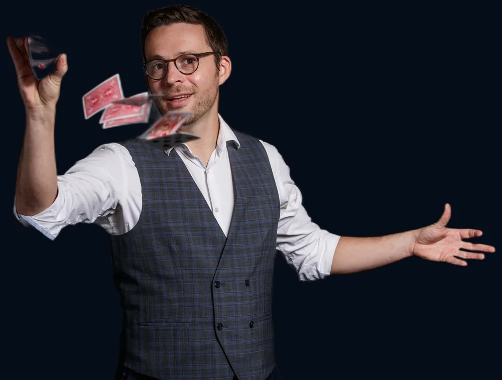 Hugo Marceau, magicien, fait jaillir des cartes à jouer d'une main à l'autre, gilet à carreaux sur fond sombre