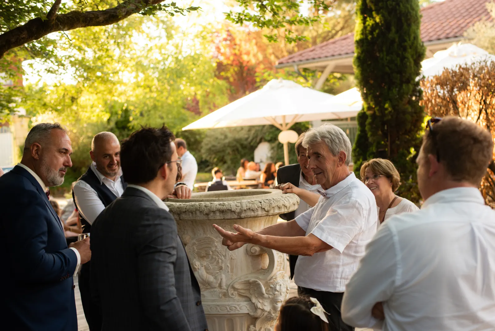 Invités d'un mariage debout en petits groupes sur la terrasse ombragée d'un domaine