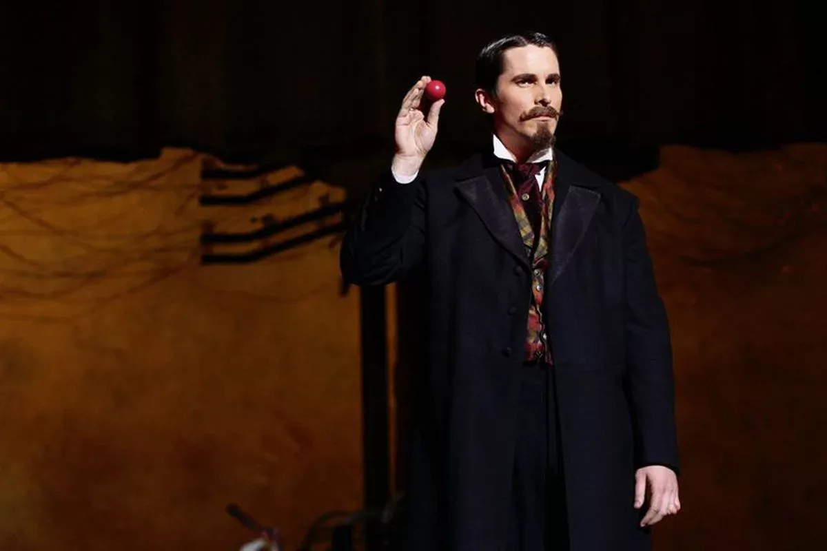 Christian Bale en Borden, sur scène, lève une petite balle rouge entre ses doigts