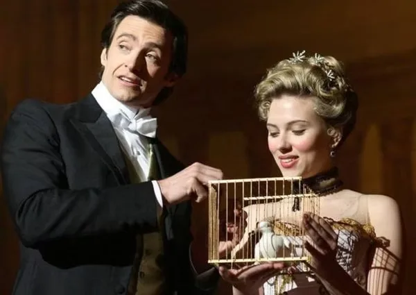 Hugh Jackman tend une cage dorée où se trouve un oiseau blanc, sous le regard de Scarlett Johansson