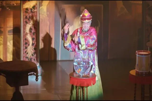 Sur scène, un vieux magicien en costume chinois fait apparaître un grand bocal d'eau avec un poisson