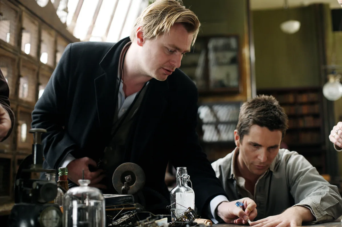Christopher Nolan penché sur un établi d'atelier avec Christian Bale, entre fioles et appareils