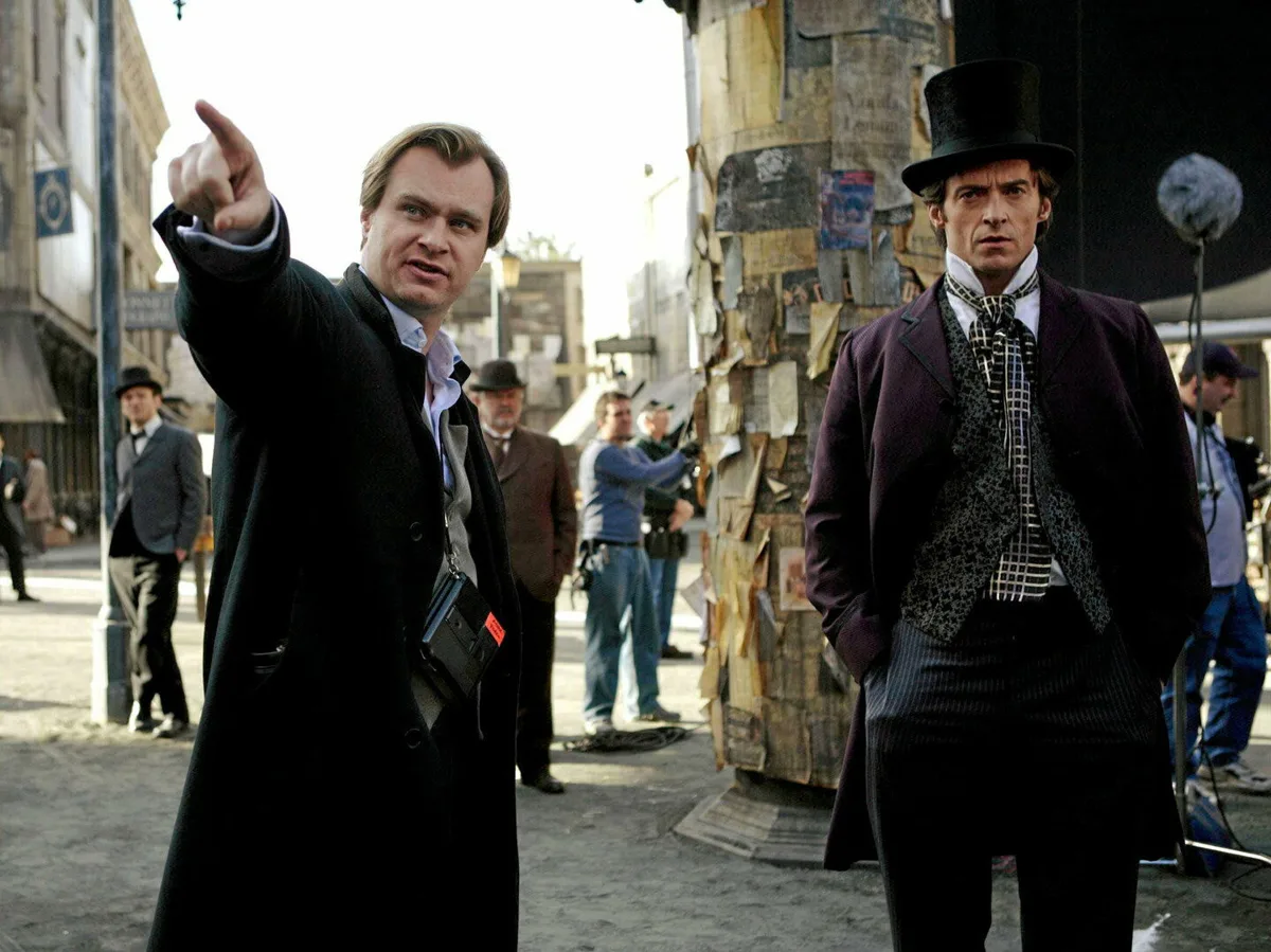 Christopher Nolan, sur le plateau, indique une direction à Hugh Jackman en costume et haut-de-forme