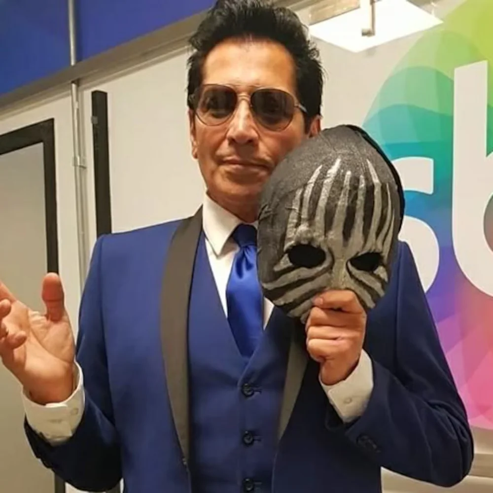 Val Valentino en costume, tenant à la main le masque qui l'a rendu célèbre